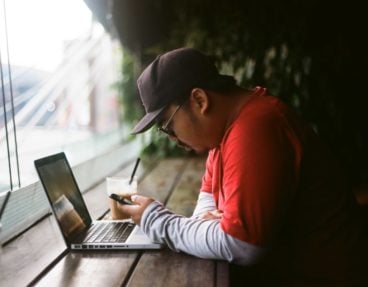 Bemannen Sie das Betrachten des Telefons und des Laptops in einem Café