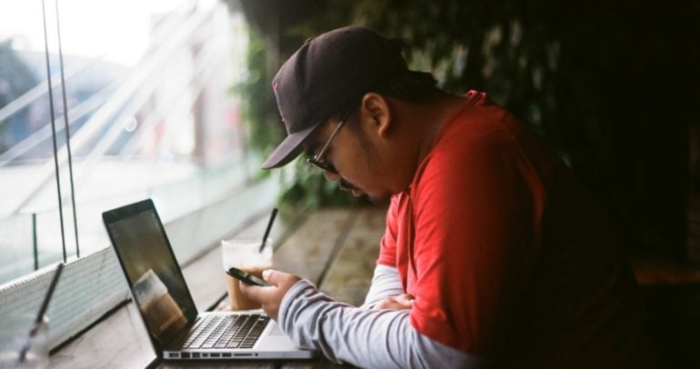 Bemannen Sie das Betrachten des Telefons und des Laptops in einem Café